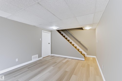 Wood-finish flooring, drop ceiling, flush mount lighting, white baseboards, and a carpeted staircase with a handrail - 155 Primrose Gardens Gardens Nw, Edmonton, AB 