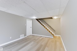 Wood-finish flooring, drop ceiling, flush mount lighting, white baseboards, and a carpeted staircase with a handrail - 