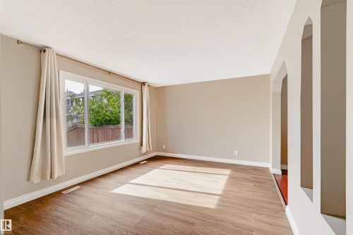 Expansive room featuring wood-finish flooring, broad windows, arched doorways, and a neutral color palette - 155 Primrose Gardens Gardens Nw, Edmonton, AB 
