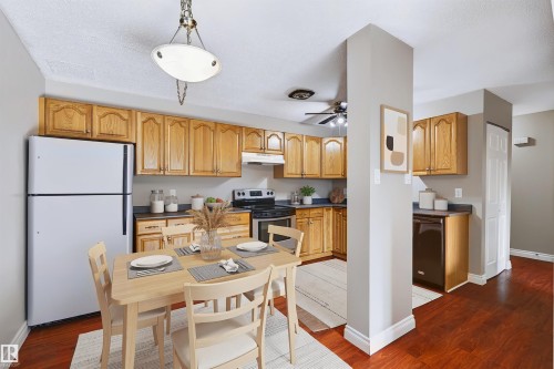 Kitchen with wood cabinetry, dark countertops, white refrigerator, black range, and wood-finish flooring - 155 Primrose Gardens Gardens Nw, Edmonton, AB 