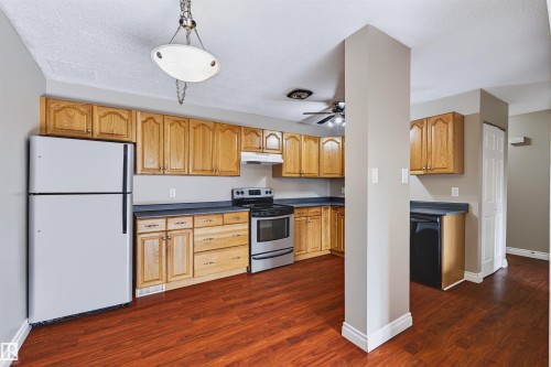 Kitchen featuring wood-finish cabinetry, dark countertops, and stainless steel appliances - 155 Primrose Gardens Gardens Nw, Edmonton, AB 