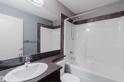 Bathroom featuring a tub/shower combination with a shower wand, a vanity with a drop-in sink, a wall-mounted mirror, and dark tile accents - 
