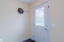 Entryway featuring a white door with decorative glass, bright interior walls, white trim, and dark floor tiles - 6717 Elston Lane Nw, Edmonton, AB 
