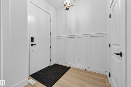 Contemporary entryway featuring wood-finish flooring, white paneled door, black hardware, and wainscoting - 11010 174A Avenue Nw, Edmonton, AB 