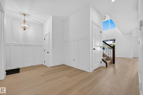Wood-finish flooring throughout, white wainscoting, gold-tone chandelier, white panel doors, and a staircase with dark wood and wrought iron railing - 11010 174A Avenue Nw, Edmonton, AB 