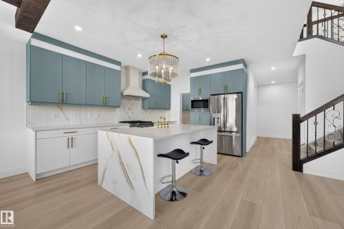 Central kitchen island with waterfall countertop, stainless steel appliances, wood-finish flooring, and a decorative wrought iron staircase - 11010 174A Avenue Nw, Edmonton, AB 