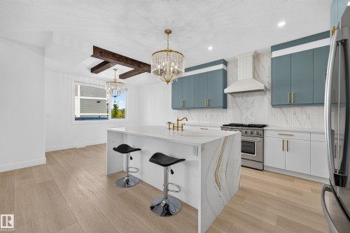 Gourmet kitchen with a large waterfall island, stainless steel appliances, decorative pendant lighting, and wood-finish flooring - 11010 174A Avenue Nw, Edmonton, AB 