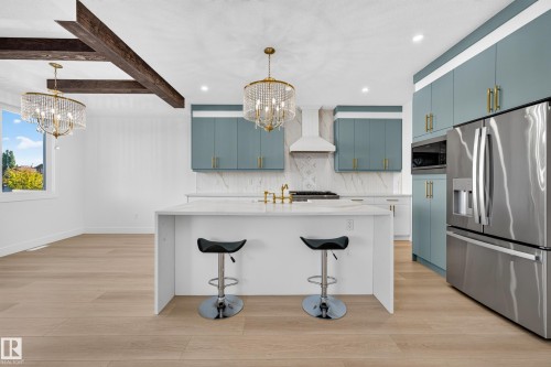Kitchen featuring a waterfall island, stainless steel refrigerator, white range hood, light wood-finish flooring, and exposed ceiling beams - 11010 174A Avenue Nw, Edmonton, AB 