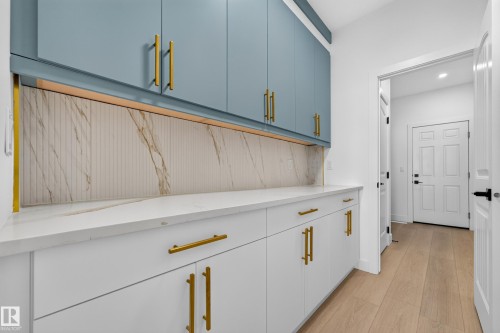 Built-in cabinetry with light blue and white finishes, gold-tone hardware, a white countertop, and wood-finish flooring - 11010 174A Avenue Nw, Edmonton, AB 