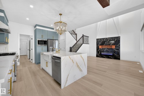 Open-concept living space with light wood-finish flooring, a contemporary black marble-look fireplace, a kitchen island with a waterfall countertop, and a crystal chandelier - 11010 174A Avenue Nw, Edmonton, AB 