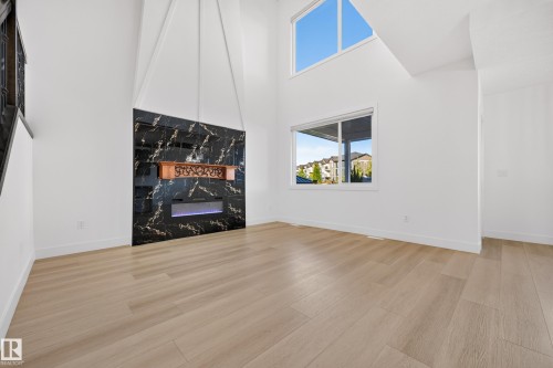 Two-story ceiling, light wood-finish flooring, black marble-look fireplace surround, linear electric fireplace, and expansive windows - 11010 174A Avenue Nw, Edmonton, AB 