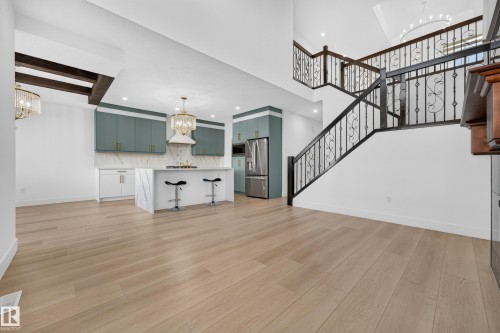 Light wood-finish flooring throughout, kitchen with two-toned cabinetry, marble-finish waterfall island, and ornate wrought iron staircase railing - 11010 174A Avenue Nw, Edmonton, AB 