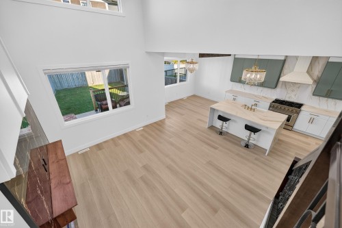 Spacious open-concept layout with light wood-finish flooring, a contemporary kitchen island, stainless steel range, and elegant decorative lighting fixtures - 11010 174A Avenue Nw, Edmonton, AB 