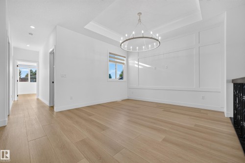 Wood-finish flooring throughout, recessed ceiling lighting, a contemporary chandelier, a window with horizontal blinds, and decorative wall paneling - 11010 174A Avenue Nw, Edmonton, AB 