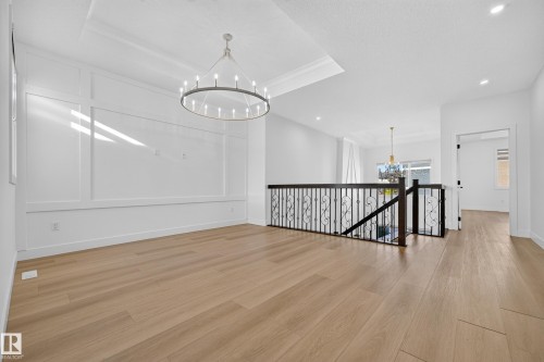 Spacious room featuring wood-finish flooring, a tray ceiling, and a prominent circular chandelier - 11010 174A Avenue Nw, Edmonton, AB 