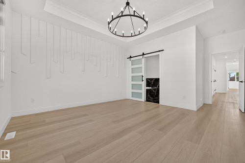 Light wood-finish flooring, accent wall with decorative paneling, recessed lighting, crown molding, and a barn door entry - 11010 174A Avenue Nw, Edmonton, AB 