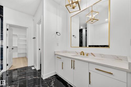 White vanity with gold hardware, white countertop with veining, rectangular undermount sink with gold faucet, black and white marble-look flooring, and a gold framed mirror - 11010 174A Avenue Nw, Edmonton, AB 