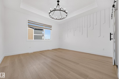 Tray ceiling with crown molding, wood-finish flooring, decorative wall paneling, modern circular chandelier, and a window with blinds - 11010 174A Avenue Nw, Edmonton, AB 