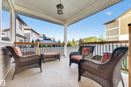 Covered outdoor patio with wood-finish flooring, white vinyl siding, and black iron railings - 11010 174A Avenue Nw, Edmonton, AB 