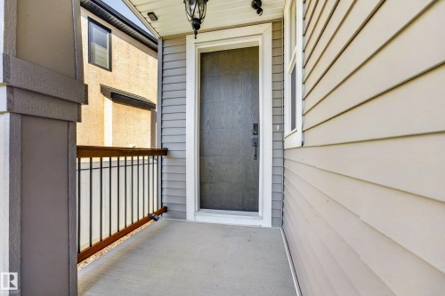 Front entry featuring a dark wood-finish door, white trim, gray shingle siding, and a concrete porch with a dark metal and wood railing - 11010 174A Avenue Nw, Edmonton, AB 