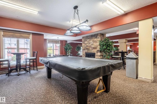 Recreational room featuring a stone-clad fireplace, patterned carpet flooring, and a multi-bulb ceiling light fixture - #230 45 Inglewood Dr, St. Albert, AB 
