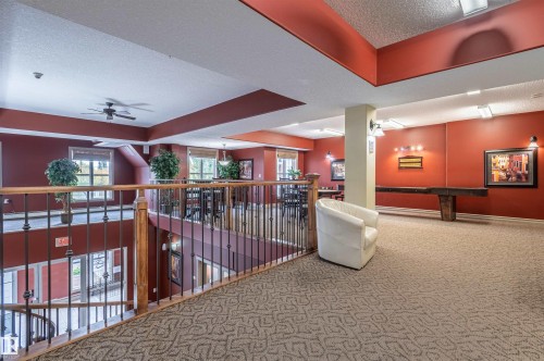 Upper-level communal area with patterned carpeting, iron railing with wood accents, recessed lighting, and wall sconces - #230 45 Inglewood Dr, St. Albert, AB 