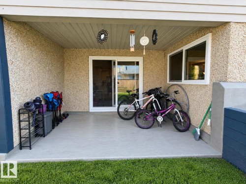 Covered patio featuring a sliding glass door, textured exterior siding, and a white framed window - #108 2624 Mill Woods Rd E Nw, Edmonton, AB 