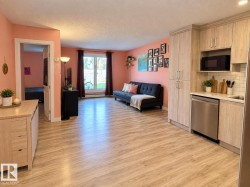 Open-concept living area with wood-finish flooring, a kitchen featuring light wood-tone cabinetry, a stainless steel dishwasher, and subway tile backsplash - 
