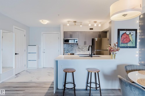 The kitchen features grey cabinetry, a stainless steel refrigerator, and a tiled backsplash - #204 11803 22 Av Sw, Edmonton, AB 