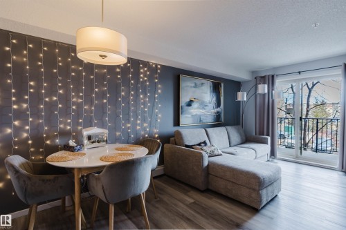 Open concept living space featuring a distinct dining area with a contemporary chandelier, and a living area with light-colored flooring and access to a balcony with metal railings - #204 11803 22 Av Sw, Edmonton, AB 
