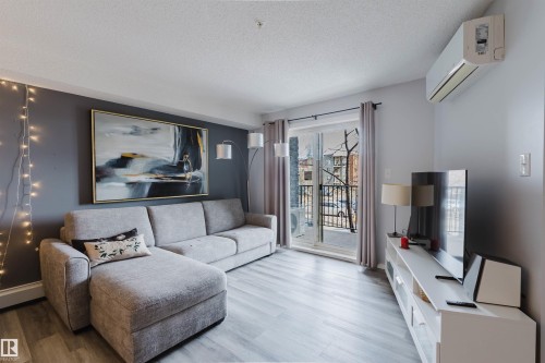 Living area featuring light-colored flooring, a sliding glass door leading to a balcony, and a wall-mounted air conditioning unit - #204 11803 22 Av Sw, Edmonton, AB 