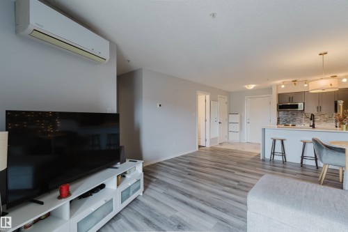 The open-concept living area features light grey walls and wood-style flooring, creating a bright and inviting atmosphere - #204 11803 22 Av Sw, Edmonton, AB 