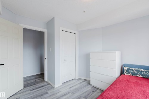 This room features light blue walls, light-toned wood-style flooring, a white bi-fold closet door, and a white interior door - #204 11803 22 Av Sw, Edmonton, AB 