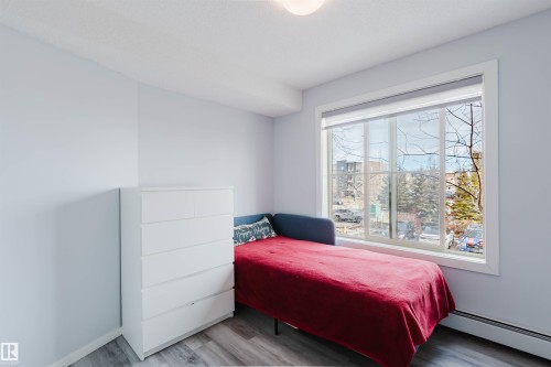 The room features light-colored walls, wood-style flooring, and a large window with white trim - #204 11803 22 Av Sw, Edmonton, AB 