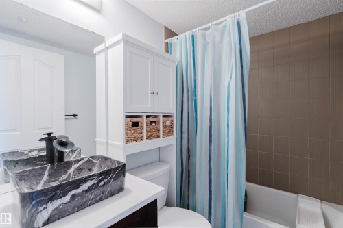 Bathroom featuring a rectangular vessel sink with a marble-like finish, a white vanity with open shelving, and a bathtub with tiled walls - #204 11803 22 Av Sw, Edmonton, AB 