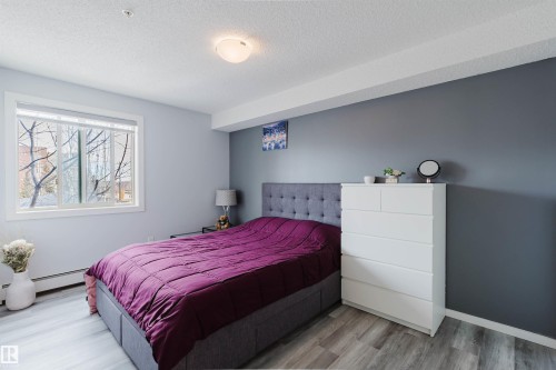 This bedroom features light-colored flooring, a large window providing natural light, and a ceiling light fixture - #204 11803 22 Av Sw, Edmonton, AB 
