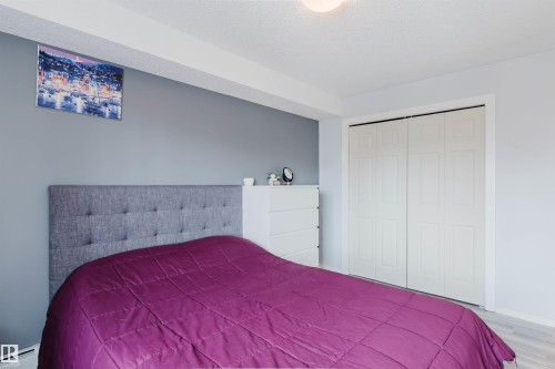 This bedroom features a light grey upholstered headboard, light-toned flooring, and a closet with bi-fold doors - #204 11803 22 Av Sw, Edmonton, AB 