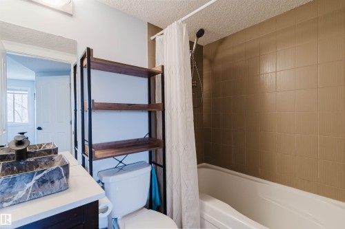 Bathroom featuring a bathtub with tiled surround, a toilet, and a vanity with a rectangular vessel sink - #204 11803 22 Av Sw, Edmonton, AB 