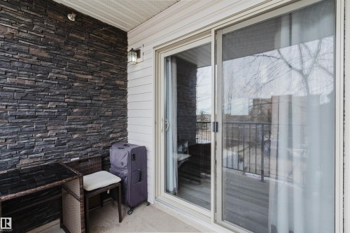 This inviting outdoor space features a stone accent wall, white siding, and a sliding glass door for seamless indoor-outdoor accessibility - #204 11803 22 Av Sw, Edmonton, AB 