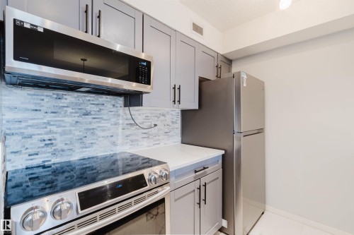 Kitchen featuring stainless steel appliances, light grey cabinetry with black hardware, white countertops, and a subway tile backsplash - #204 11803 22 Av Sw, Edmonton, AB 