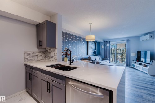 Kitchen area featuring gray cabinetry, a mosaic tile backsplash, a large kitchen island with a dark sink, and stainless steel appliances - #204 11803 22 Av Sw, Edmonton, AB 