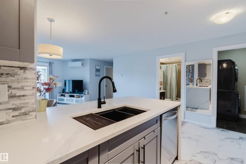 The kitchen features a large island with a black sink and faucet, complemented by a white countertop with grey veining - #204 11803 22 Av Sw, Edmonton, AB 