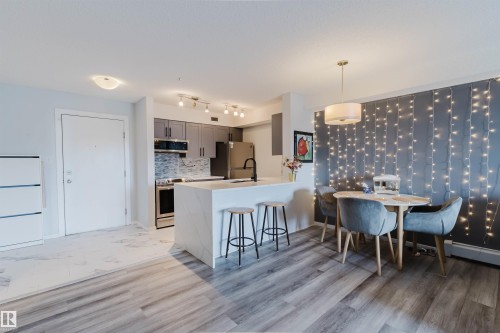 Open concept living area featuring wood-look flooring and a kitchen with stainless steel appliances, grey cabinetry, and a white marble-look island - #204 11803 22 Av Sw, Edmonton, AB 