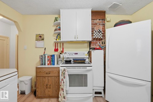 White upper cabinetry, exposed brick detail, white appliances, and wood-finish flooring - 9628 100A Street Nw, Edmonton, AB 