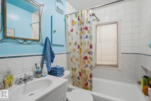 Bathroom featuring a vanity with a white basin sink, polished chrome faucet, a mounted mirror, and a built-in bathtub with white tile surround - 9628 100A Street Nw, Edmonton, AB 
