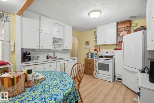 Kitchen featuring white cabinetry, light wood-finish flooring, and a brick-finish accent wall - 9628 100A Street Nw, Edmonton, AB 