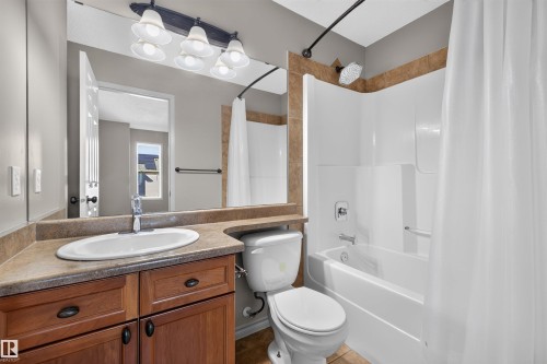 Bathroom featuring a vanity with a drop-in sink, wood-finish cabinetry, a full-width mirror, a toilet, and a shower-tub combination with tile surround - 6116 8 Avenue Sw, Edmonton, AB 