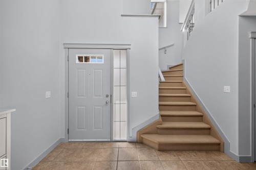 Entryway with tile flooring, a front door with decorative glass, and a carpeted staircase featuring a railing - 6116 8 Avenue Sw, Edmonton, AB 