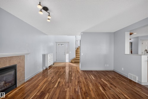 Wood-finish flooring throughout, featuring a fireplace with tile surround, modern ceiling light fixture, and an entry door with glass inserts - 6116 8 Avenue Sw, Edmonton, AB 