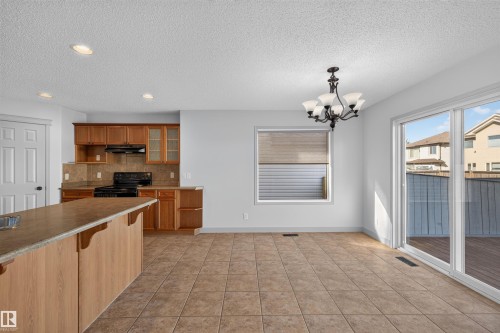 Open-concept living space with tile flooring, a kitchen featuring wood cabinetry and a large island, an overhead chandelier, and sliding glass doors to the exterior - 6116 8 Avenue Sw, Edmonton, AB 
